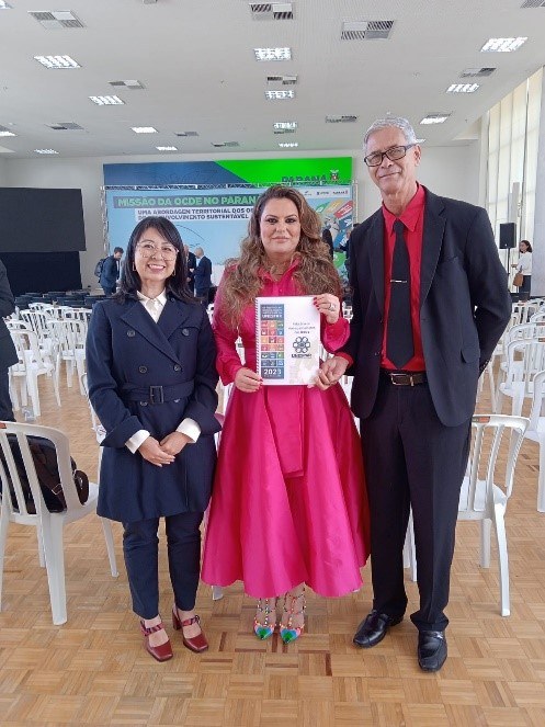 Professores Sebastião e Gisele entregando o Relatório de Acompanhamento dos ODS´s da Unespar para Kely Guimarães, Superintendente Geral de Desenvolvimento Econômico e Social do Paraná.